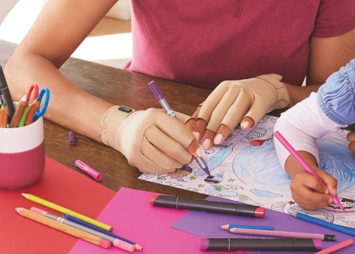 Mujer coloreando un dibujo mientras lleva los guantes para artritis Actimove Arthritis Care para aliviar los primeros síntomas.  Mujer coloreando un dibujo mientras lleva los guantes para artritis Actimove Arthritis Care para aliviar los primeros síntomas.